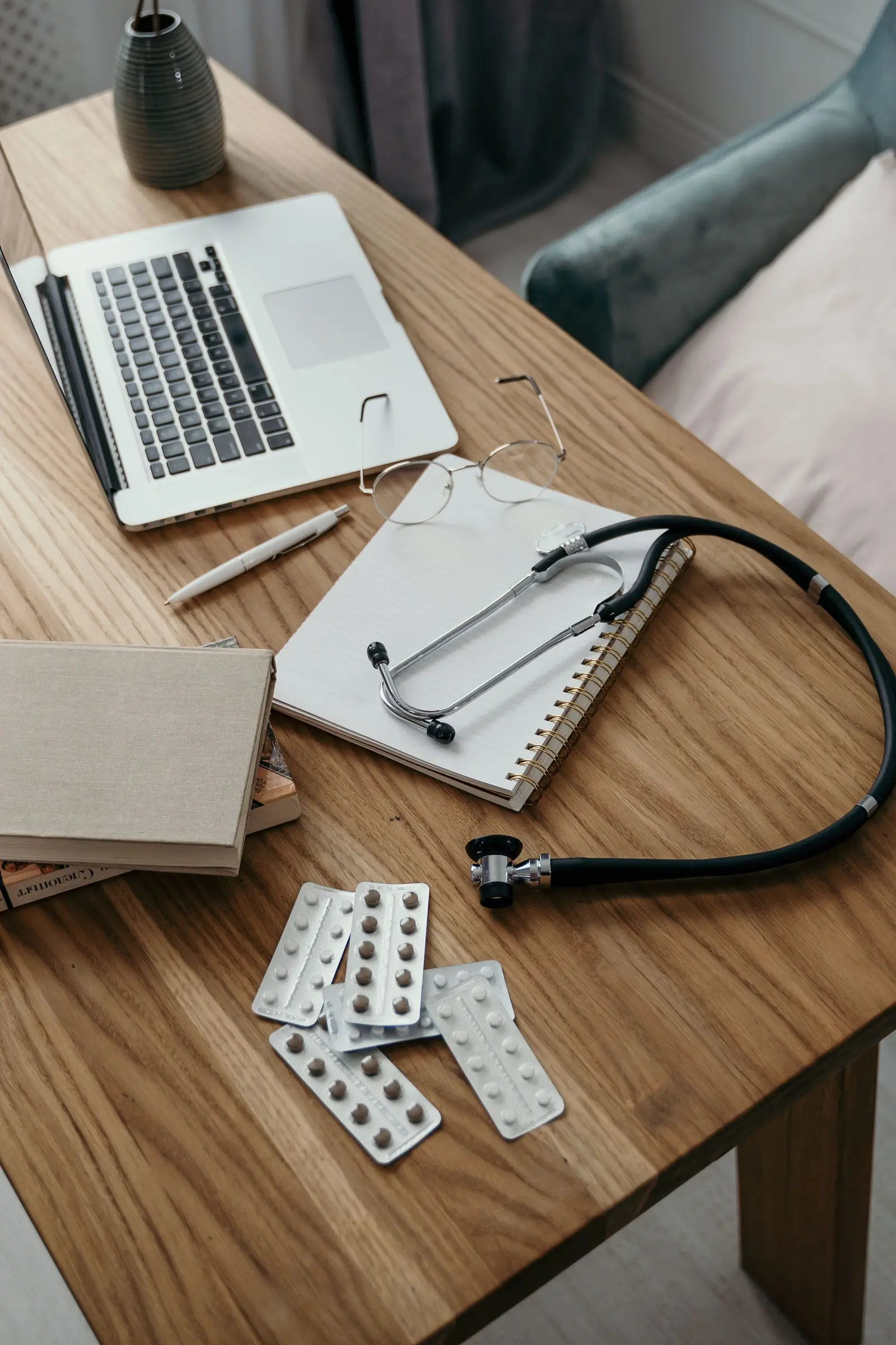 A stethoscope, notebook and laptop on a warm wooden desk.