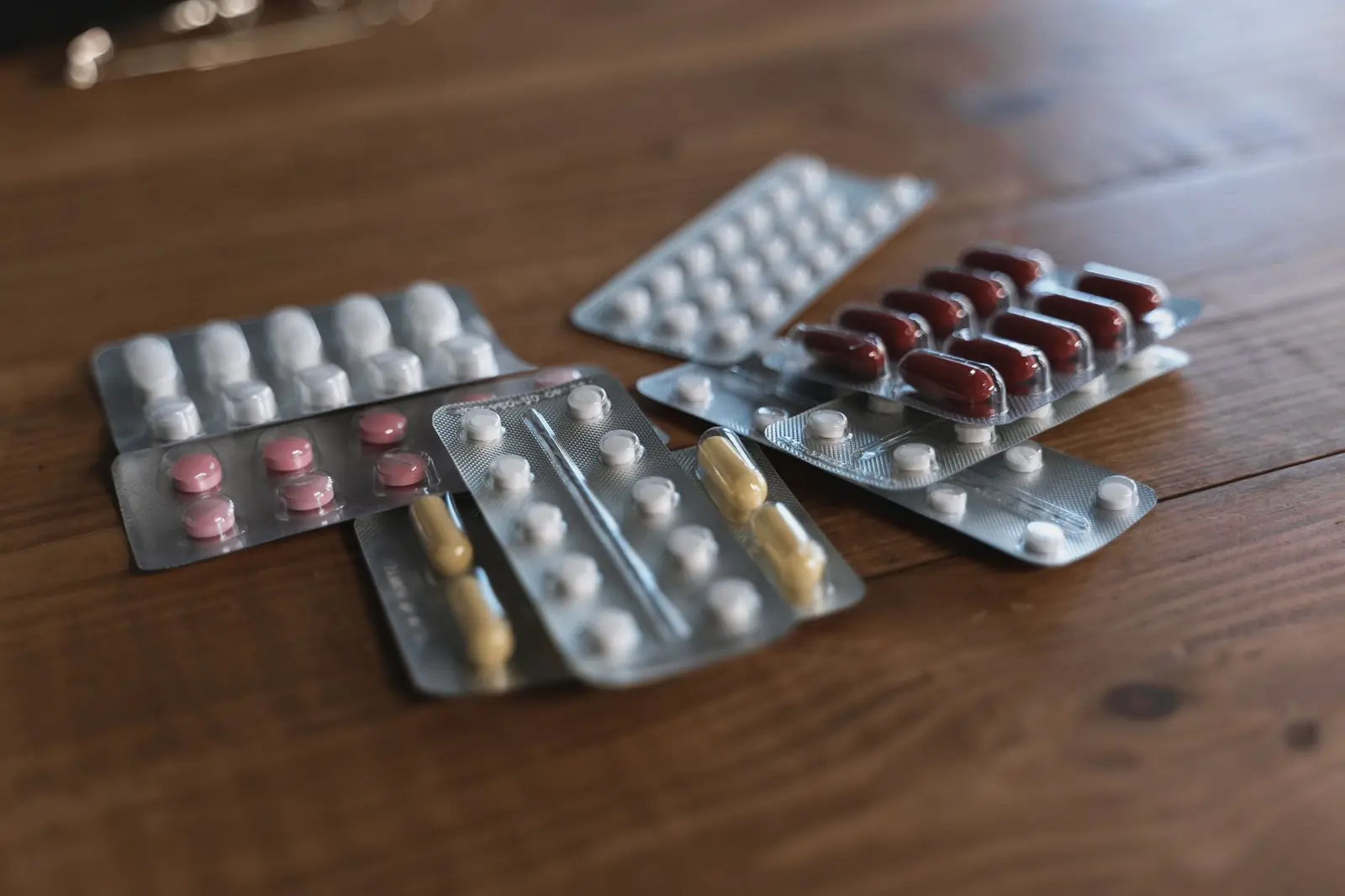 Several blister packs of capsules and tablets lying on a warm wooden table