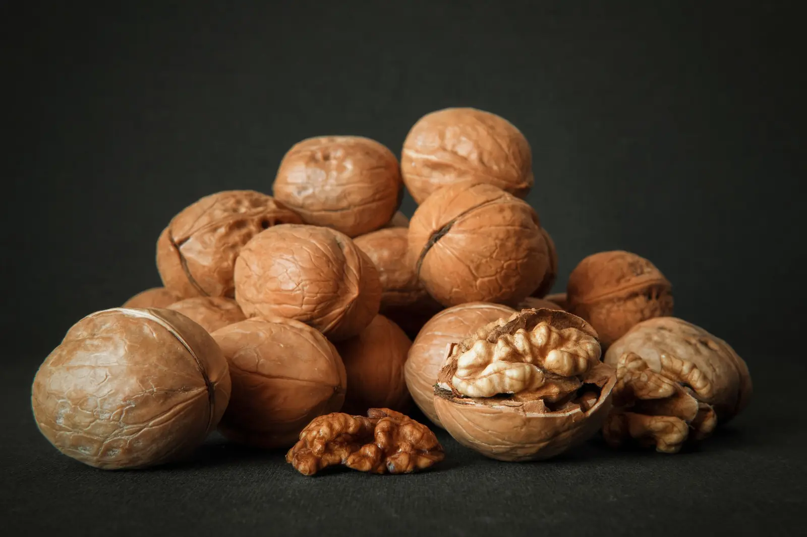 A small pile of whole walnuts, one cracked open, against a dark background