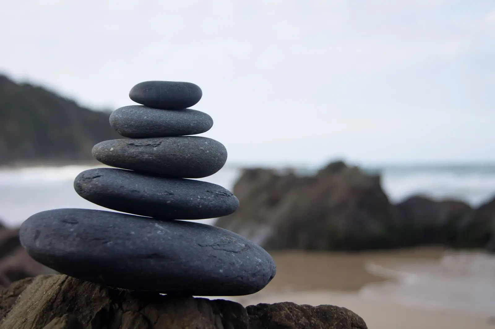 A neat stack of smooth dark stones balanced on a rock above a quiet beach