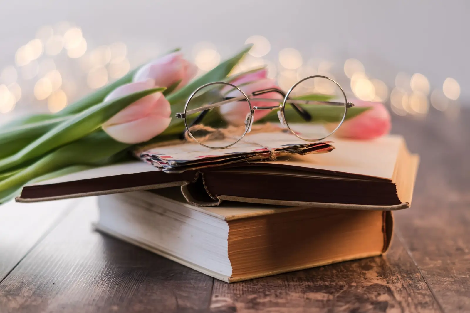 Round reading glasses resting on pink tulips and a stack of old books