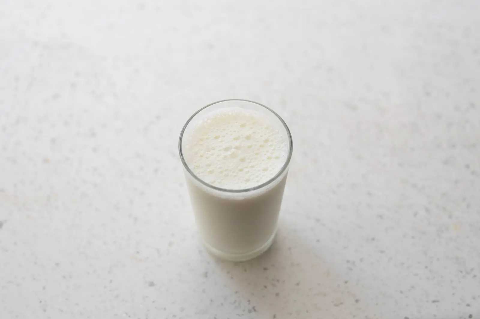 A single glass of milk on a pale speckled stone countertop