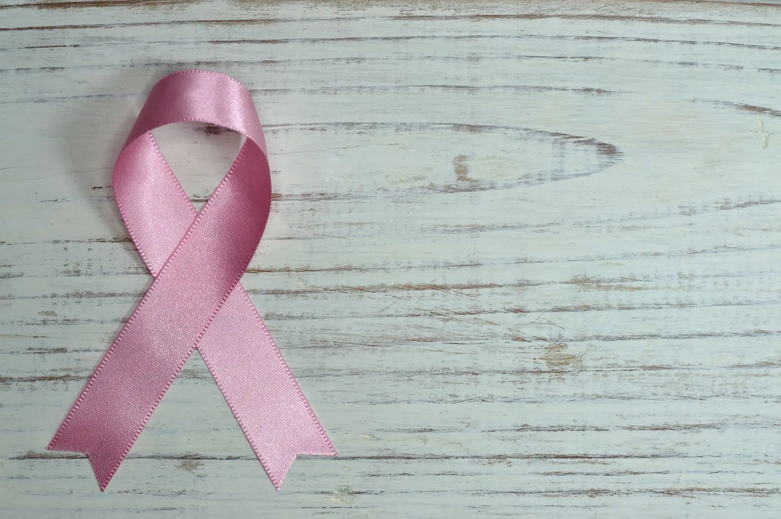 A pink awareness ribbon lying on a pale teal painted wooden surface