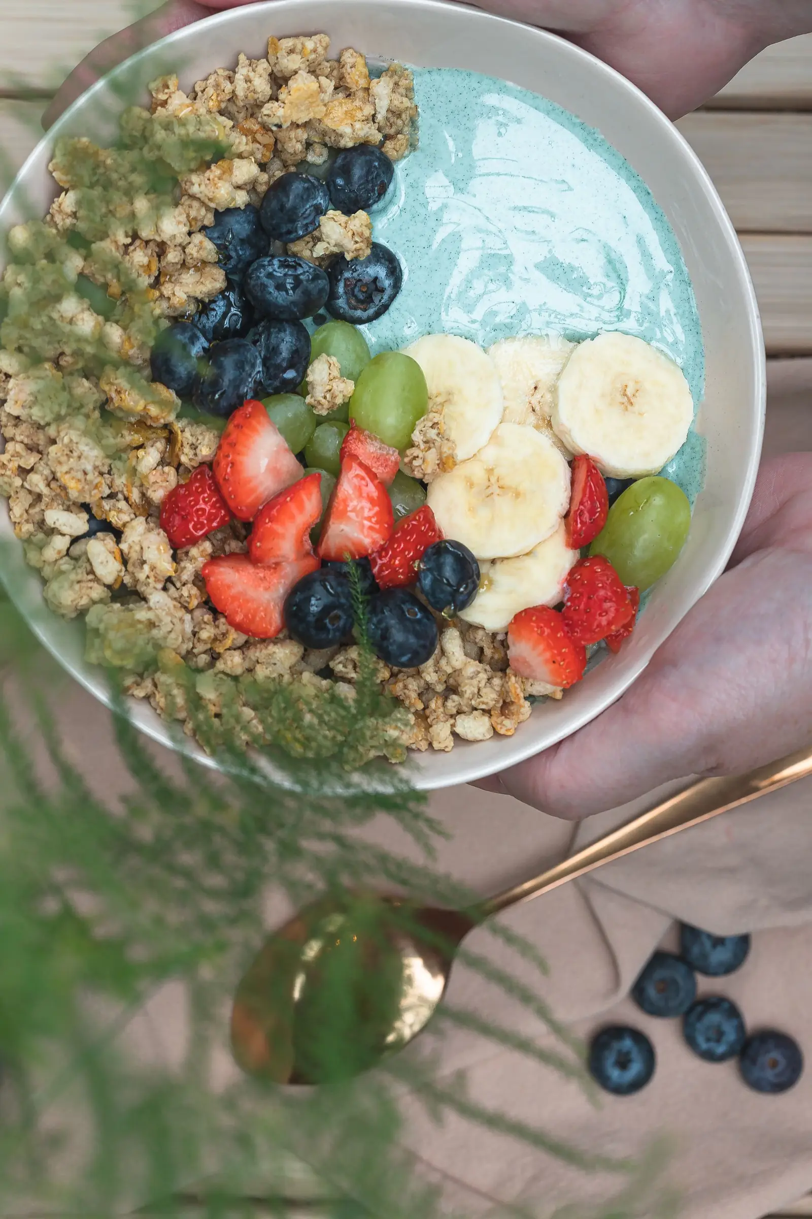 A bowl of fruit, granola and berries on a wooden table.