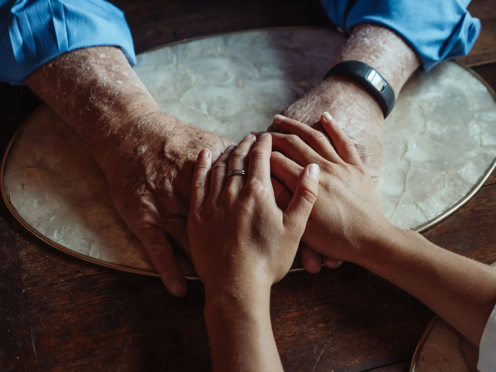 An older person's hands clasped with a younger person's hands on a round wooden table