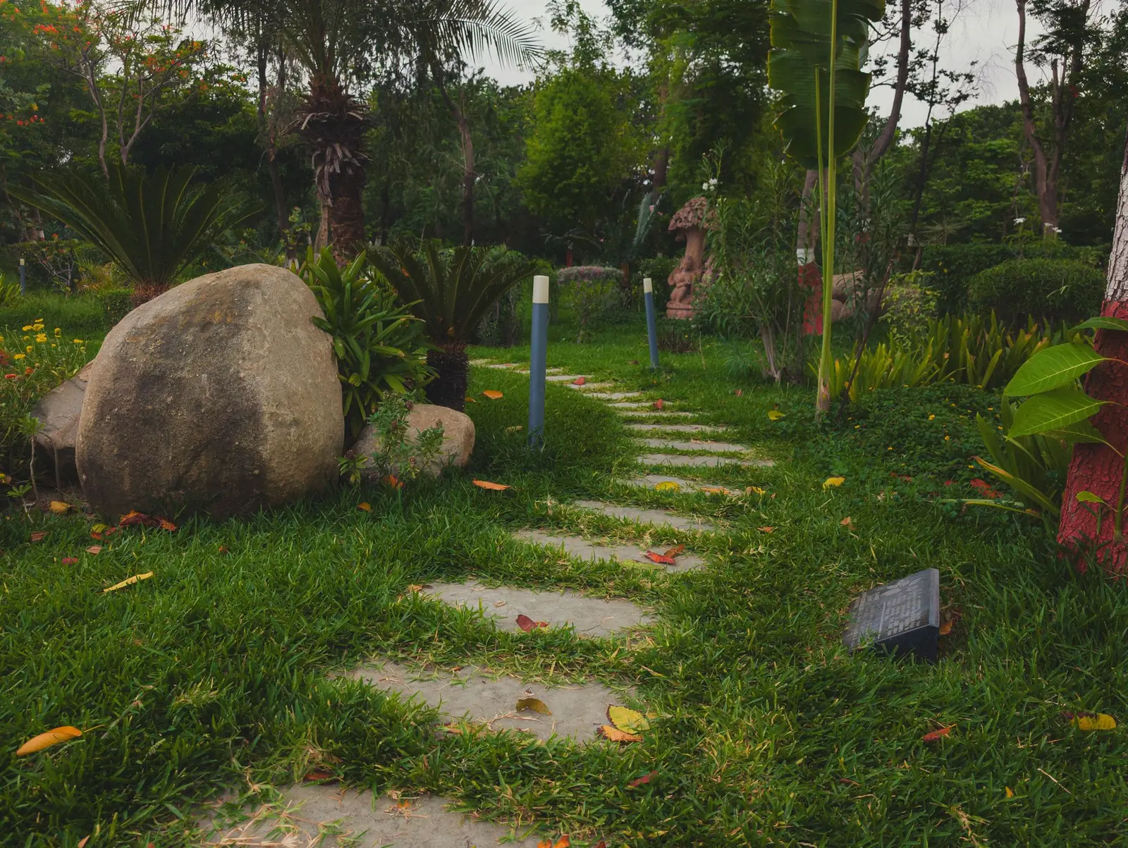 Flat stepping stones leading through green grass in a leafy garden beside a large boulder
