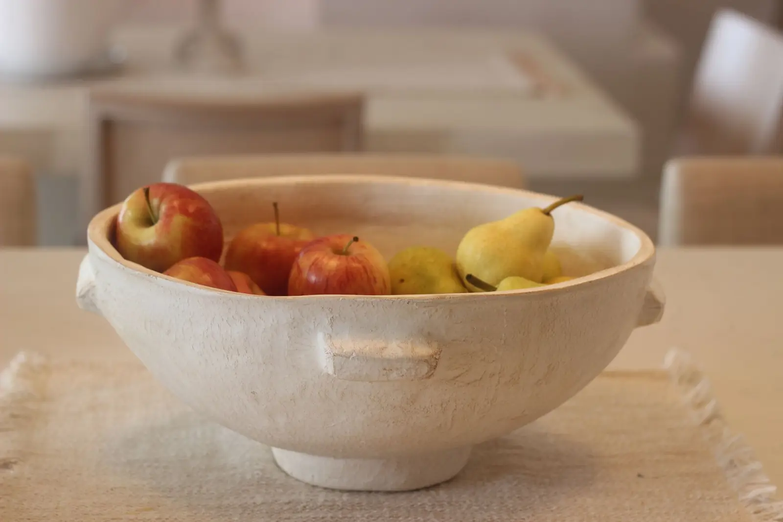 A cream ceramic bowl of red apples and yellow pears on a linen cloth on a light table