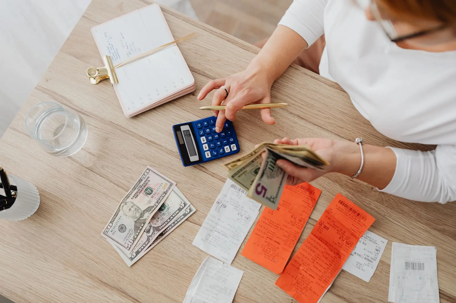 Overhead view of hands using a calculator with cash and receipts on a wooden table