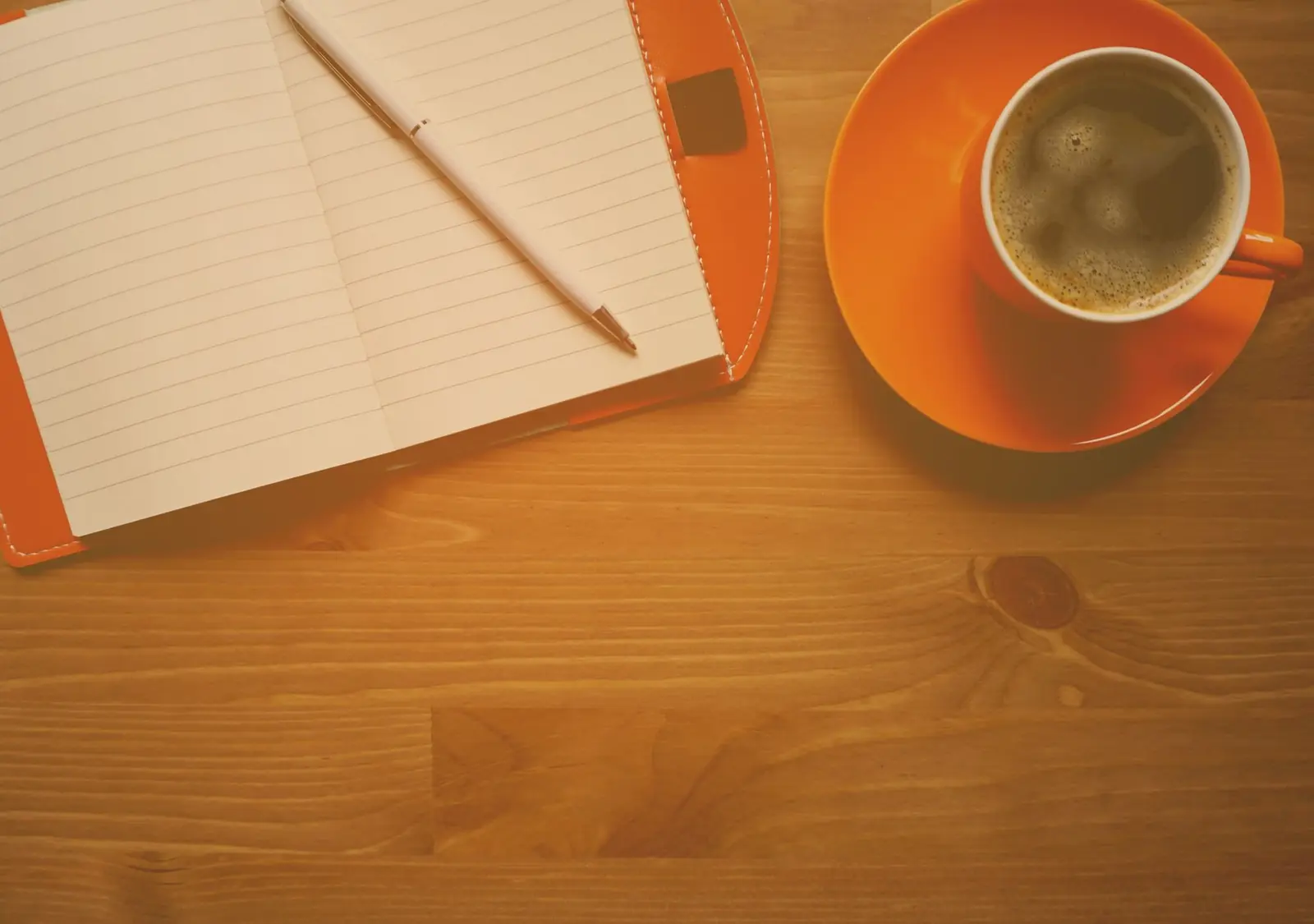 An open lined notebook with a pen beside a cup of coffee on a warm wooden table