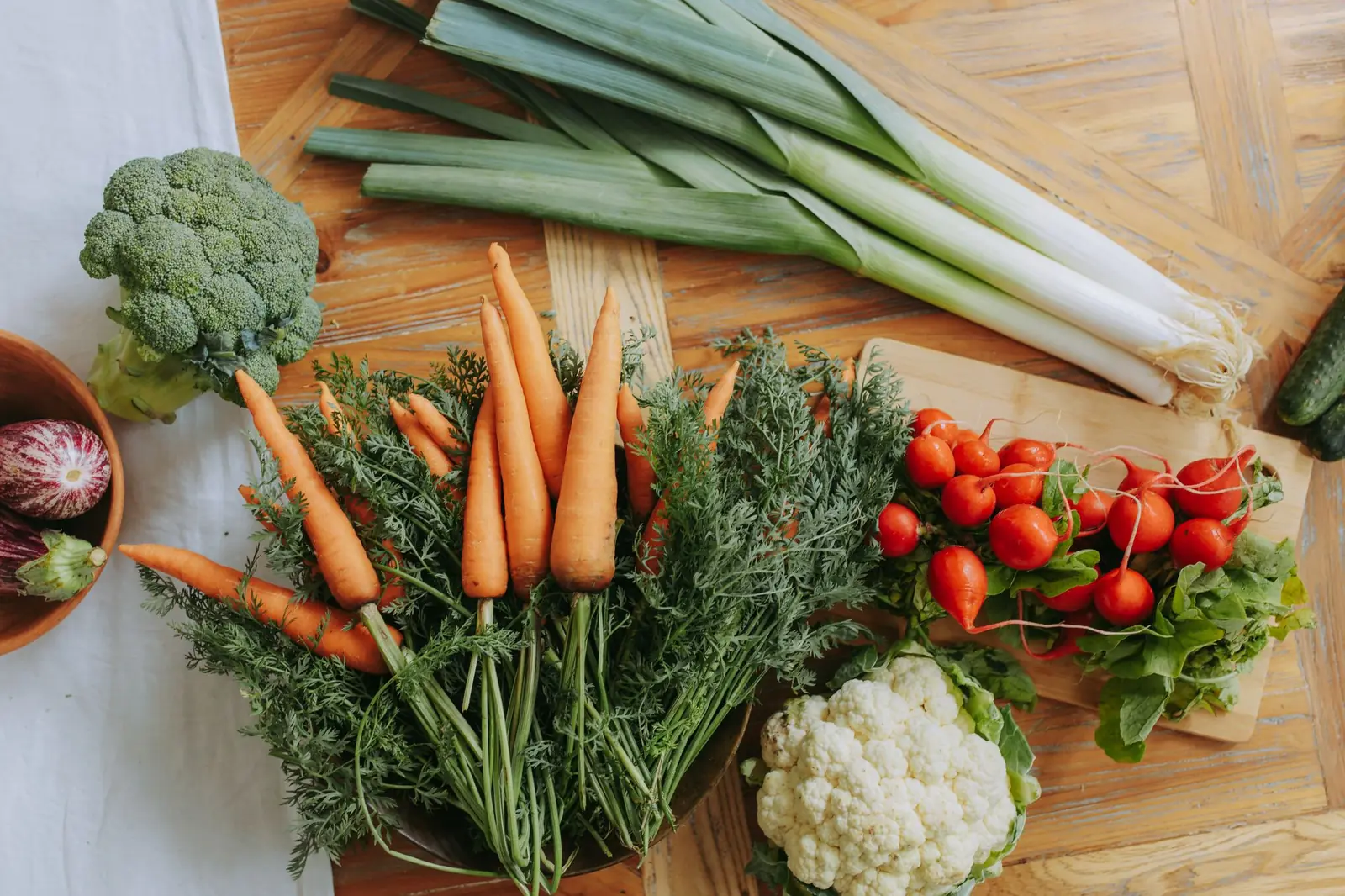 Carrots, leeks, broccoli, cauliflower, radishes and cherry tomatoes laid out on a light wooden table