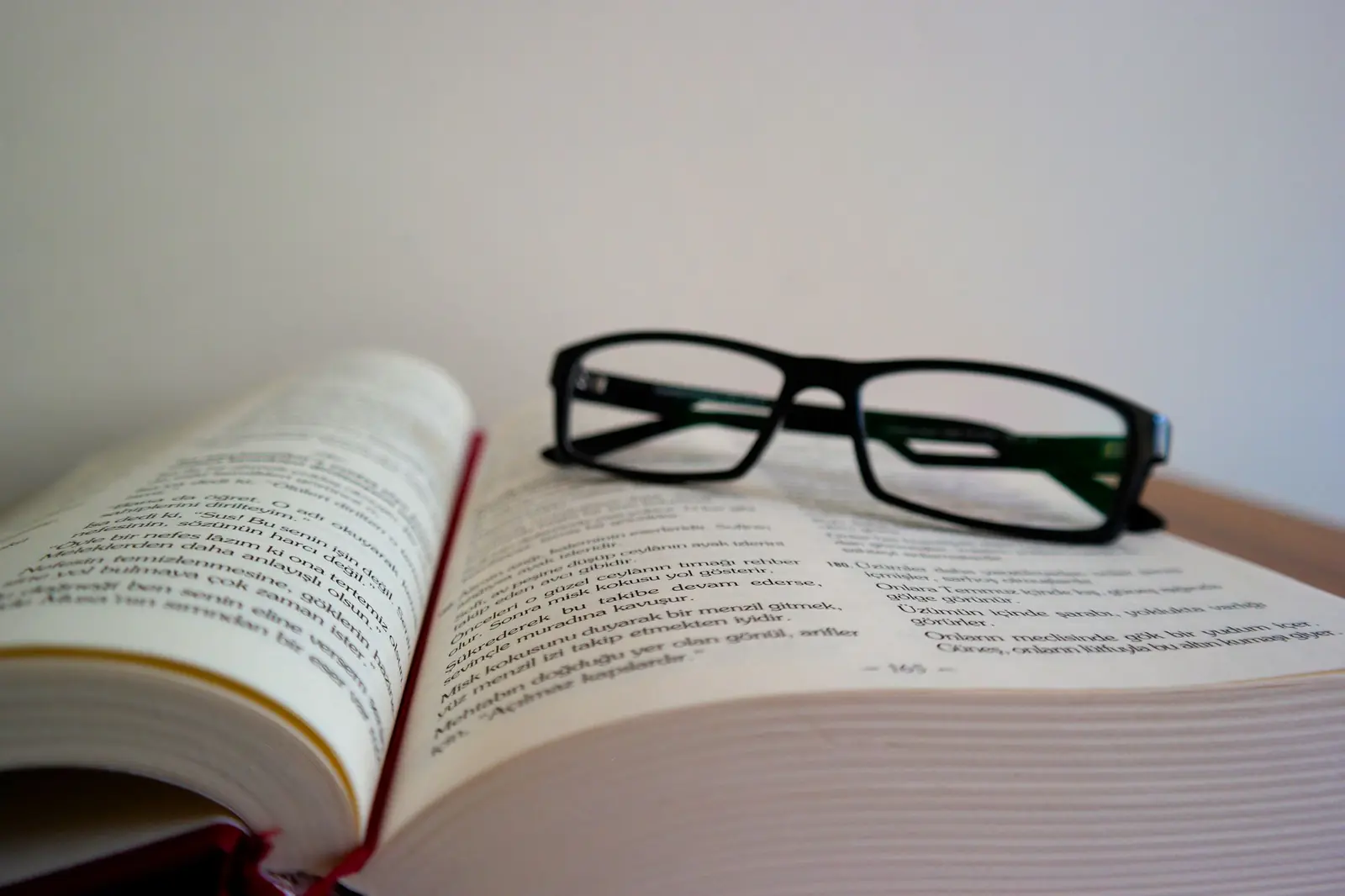 Black-framed eyeglasses resting on an open book against a pale wall