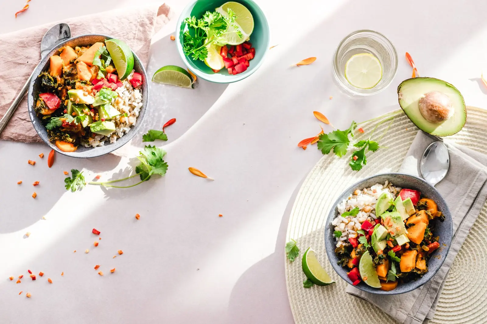 Bowls of grain and vegetable salad with avocado and lime on a sunlit table