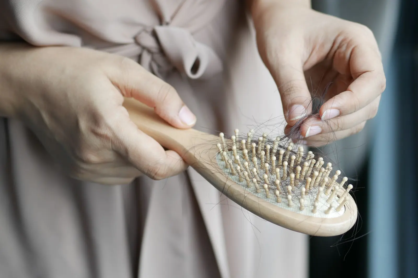 Hands pulling loose strands of hair from the bristles of a wooden hairbrush