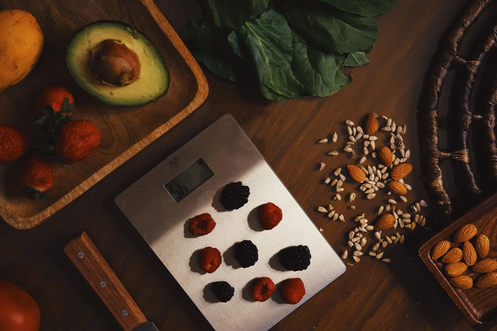 Avocado, strawberries, almonds, seeds and fresh berries arranged on a dark wooden table