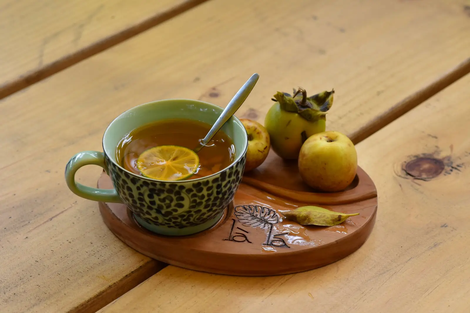 A cup of tea with a lemon slice and small apples on a wooden tray