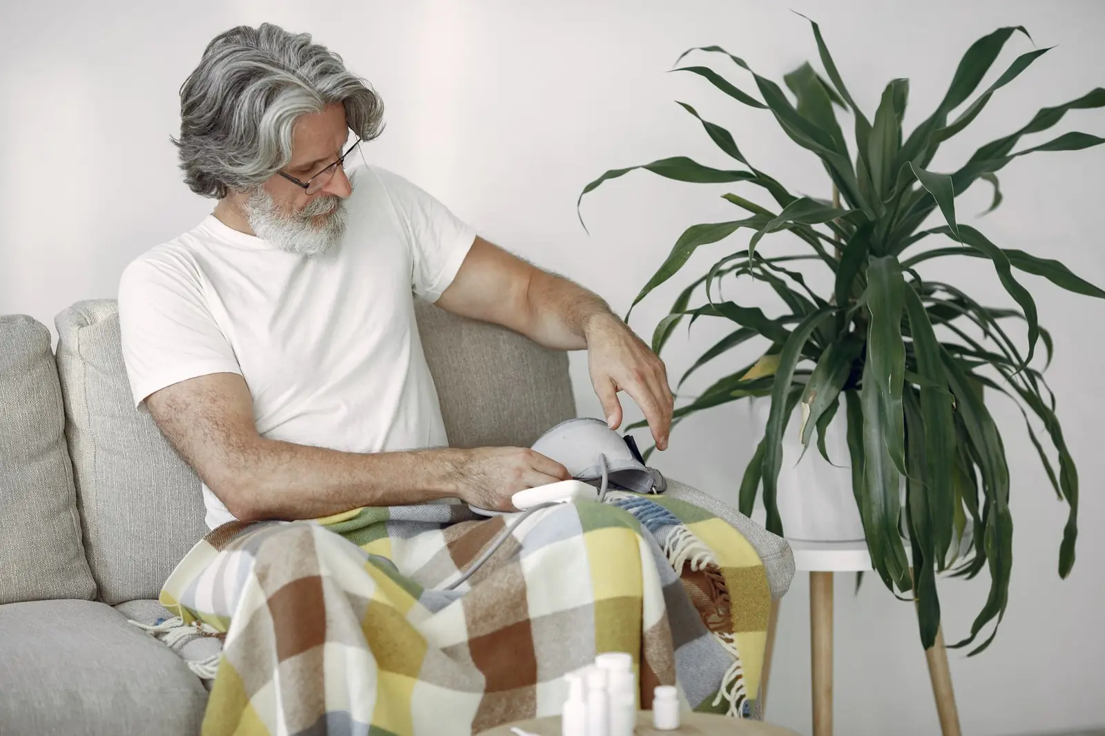An older man on a sofa fitting a blood pressure cuff to his arm at home