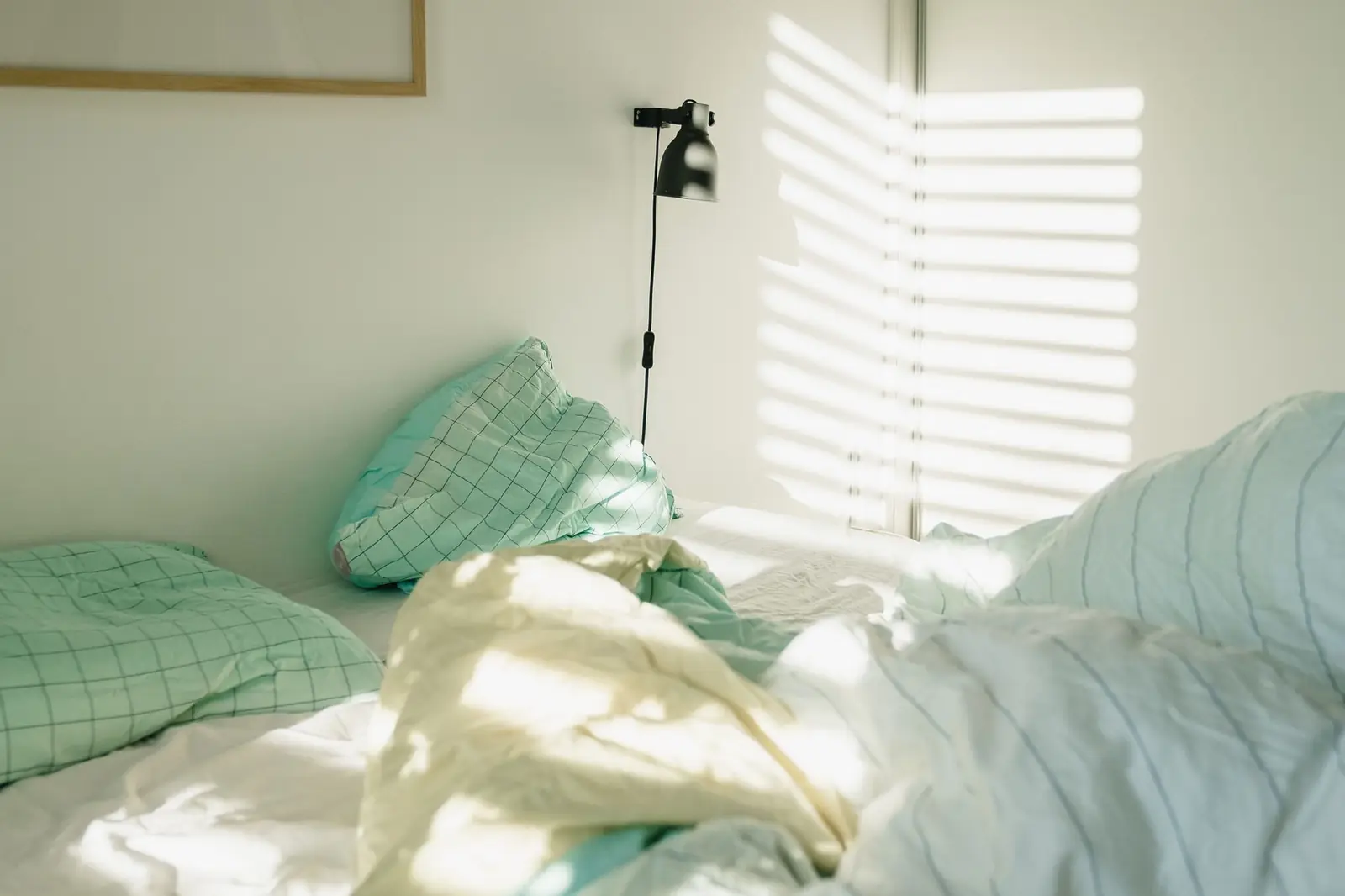 A softly made bed with mint and cream linens in a quiet room lit by morning sun