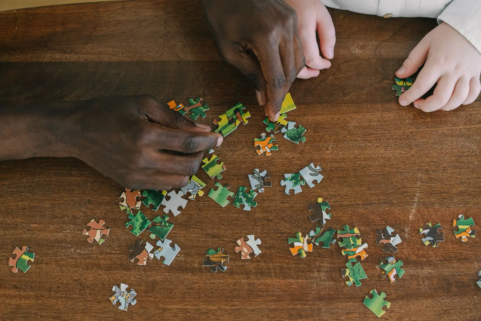Two people's hands working on a jigsaw puzzle together on a wooden table