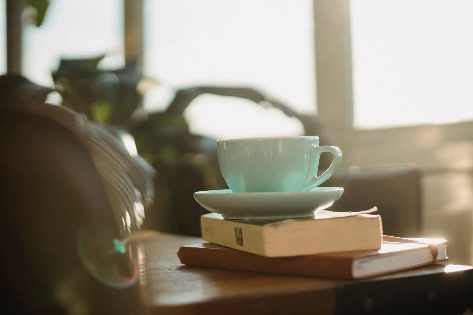 A pale green cup and saucer resting on two books on a table in soft window light