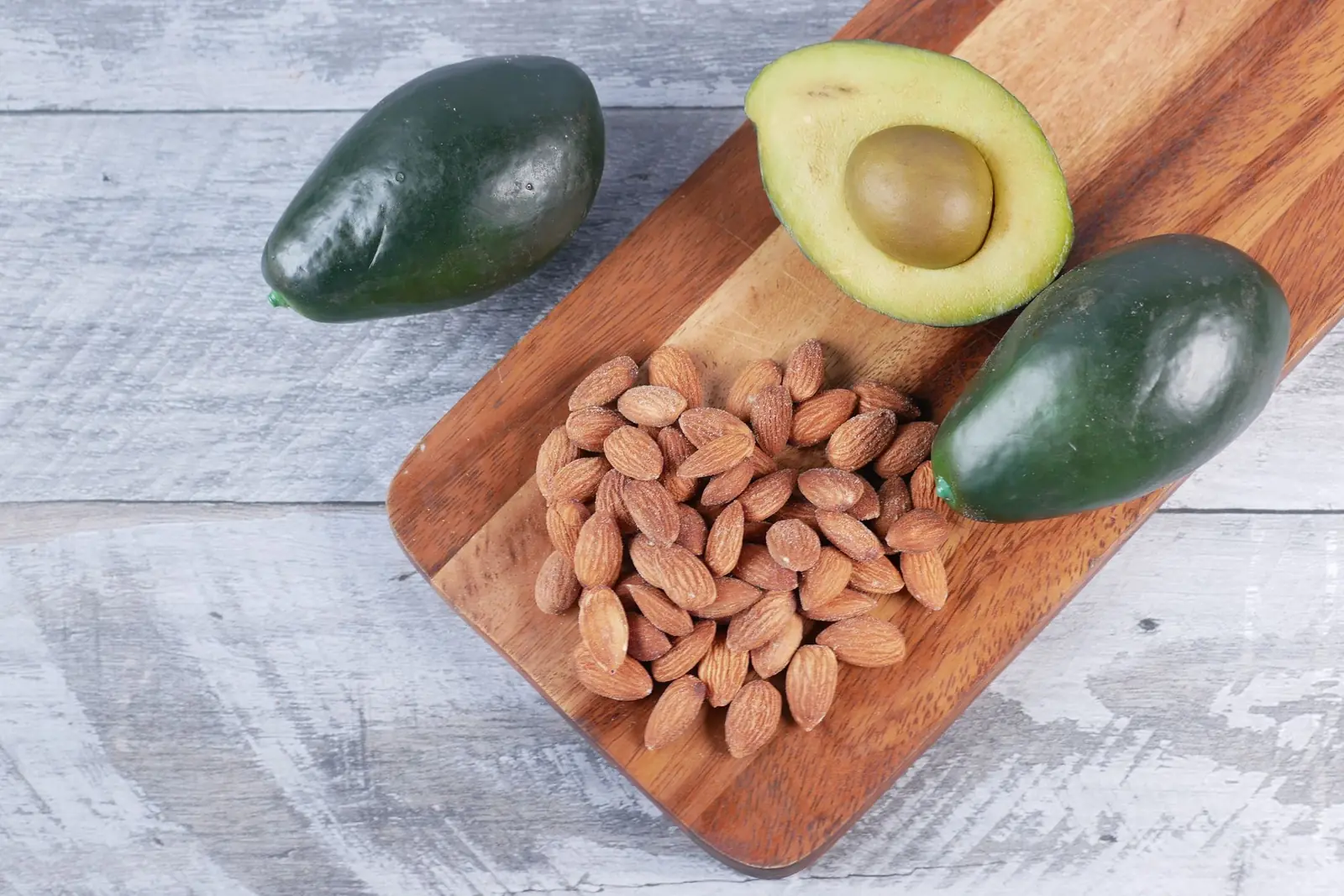 Whole and halved avocados with a pile of almonds on a wooden cutting board