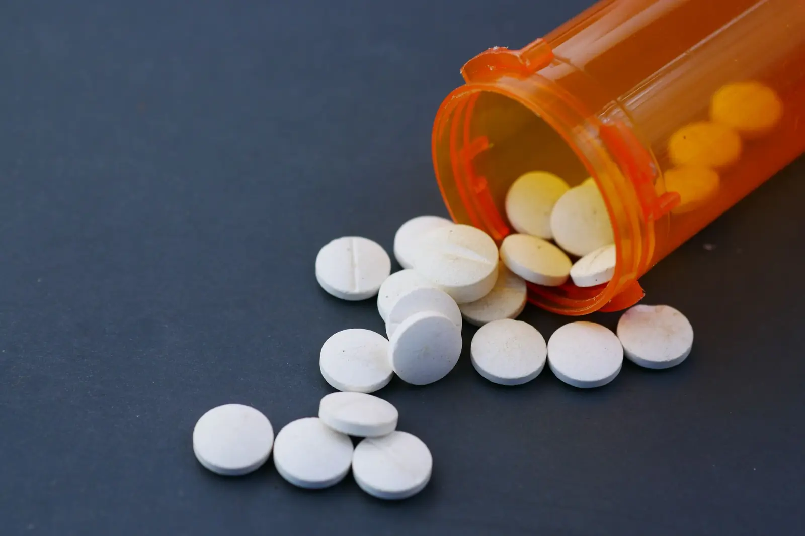 White tablets spilling from an orange pill bottle onto a dark blue surface