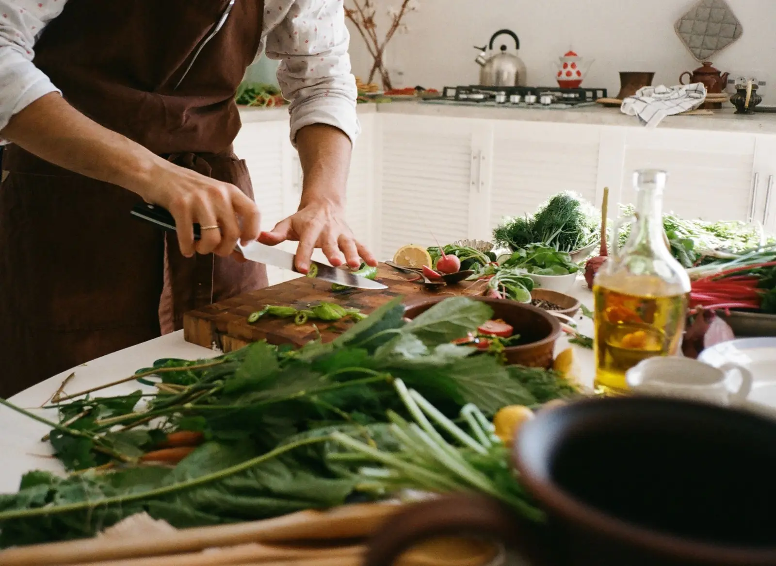 A person slicing fresh greens on a cutting board in a sunny kitchen with olive oil nearby
