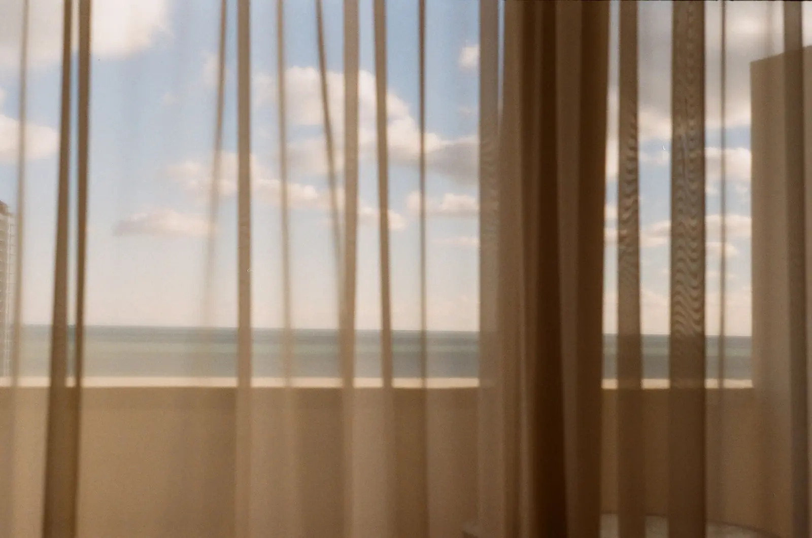 Sheer beige curtains in front of a window with a view of the sea and sky