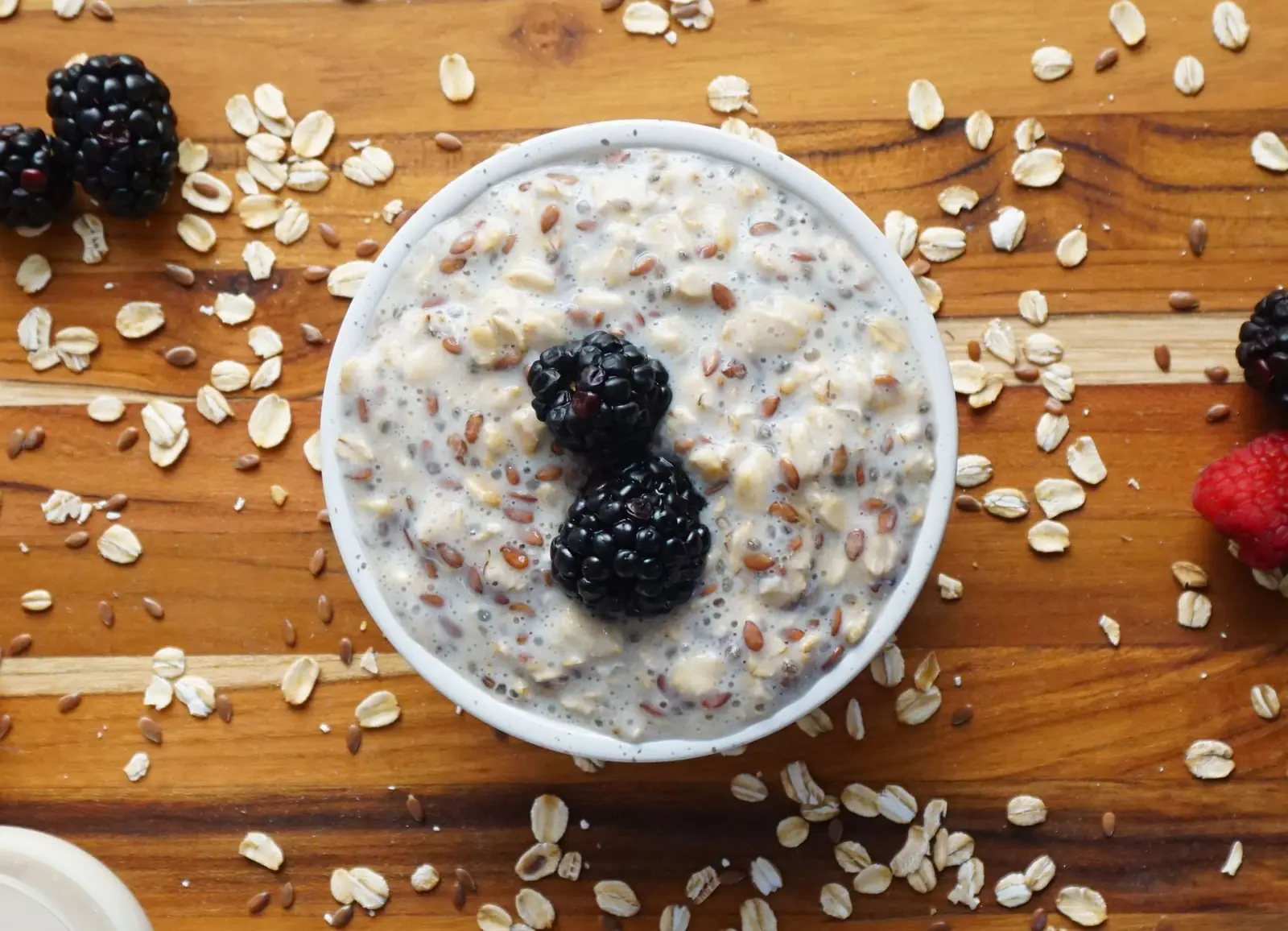 A bowl of oatmeal topped with blackberries on a wooden board scattered with oats