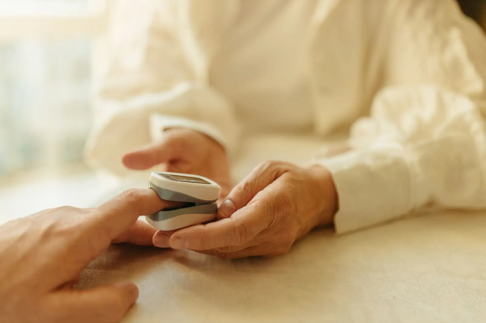 An older adult's hands resting on a table with a pulse oximeter clipped to one fingertip