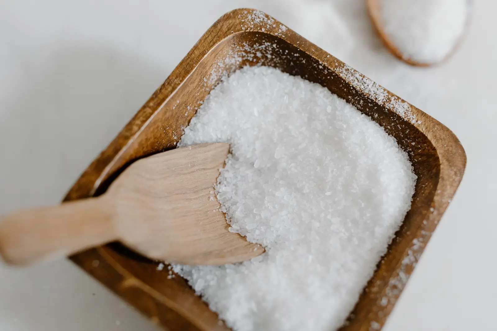 Coarse white salt heaped in a square wooden bowl with a small wooden scoop