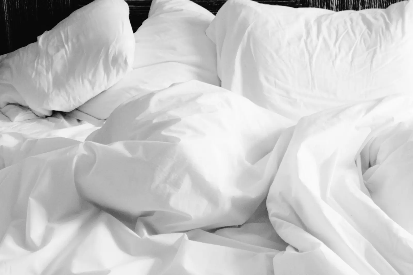 Rumpled white sheets and pillows on a bed in soft morning light