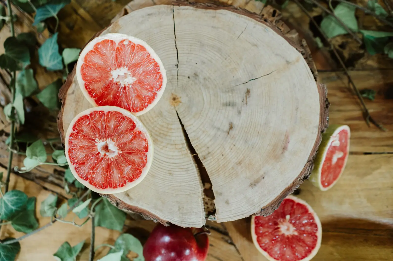 Halved pink grapefruit on a round slice of wood surrounded by ivy leaves