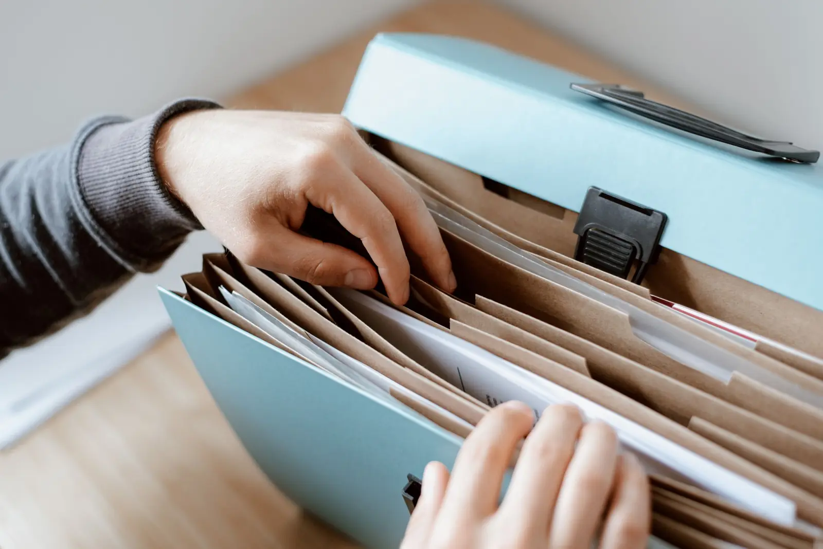 Hands sorting through papers in a pale blue accordion file folder on a table