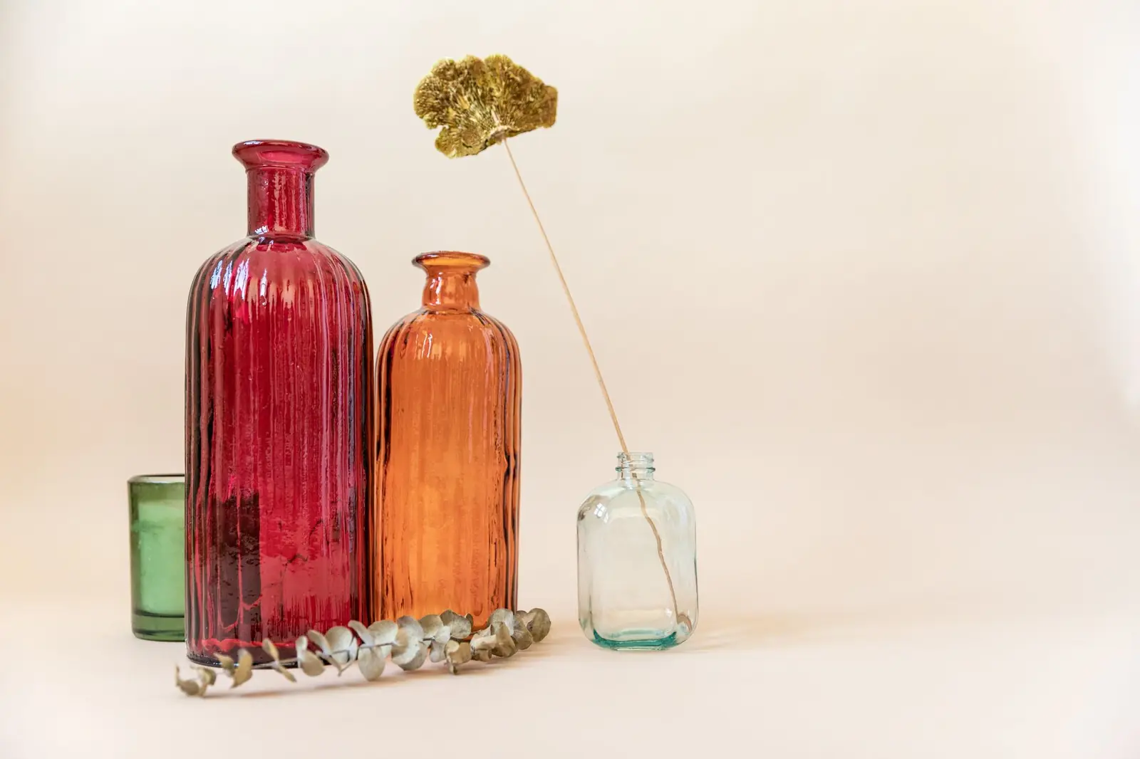Red, amber and clear glass bottles with a dried flower stem and eucalyptus on a cream backdrop