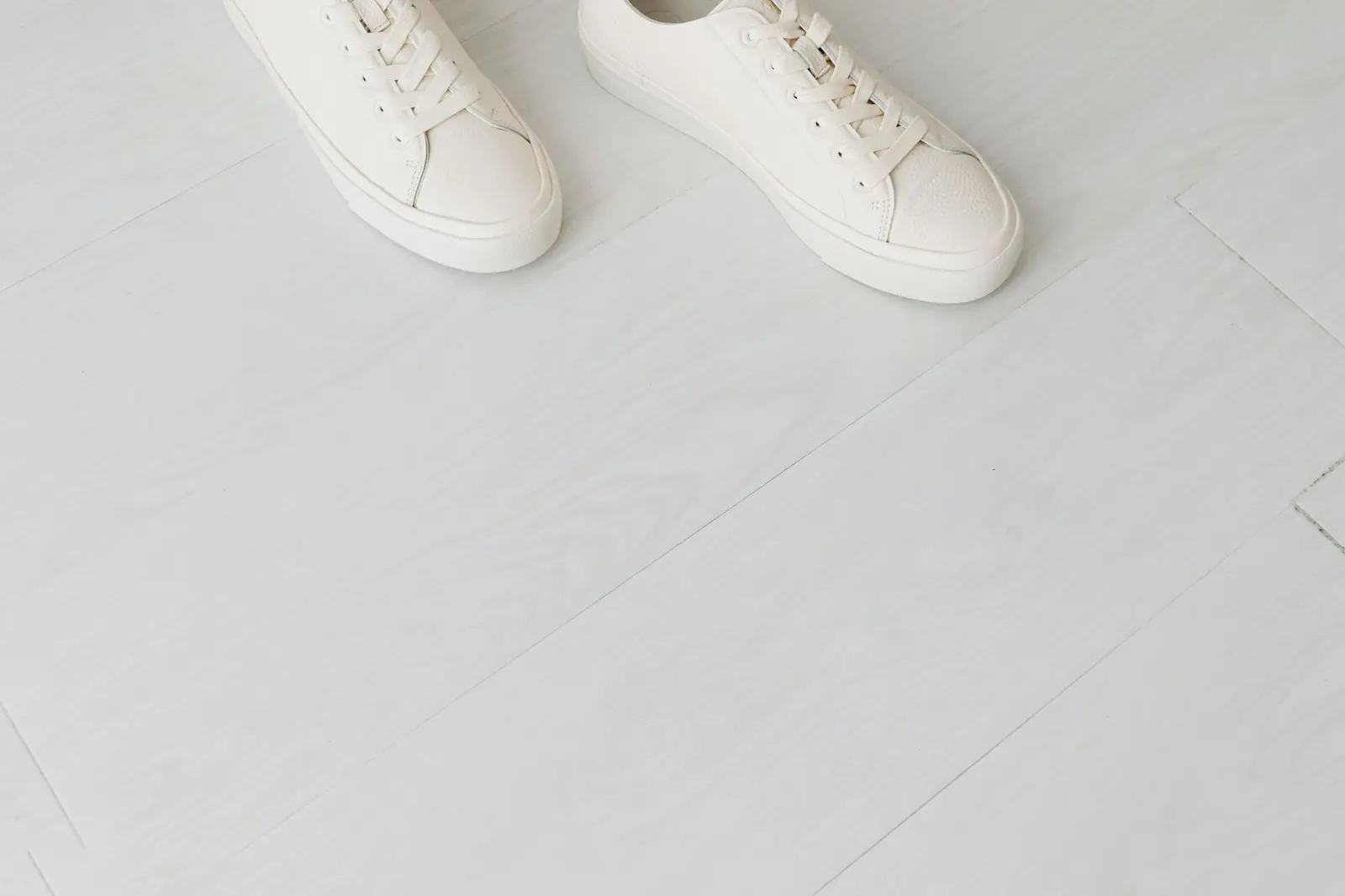 A pair of plain white sneakers standing on a pale wooden floor