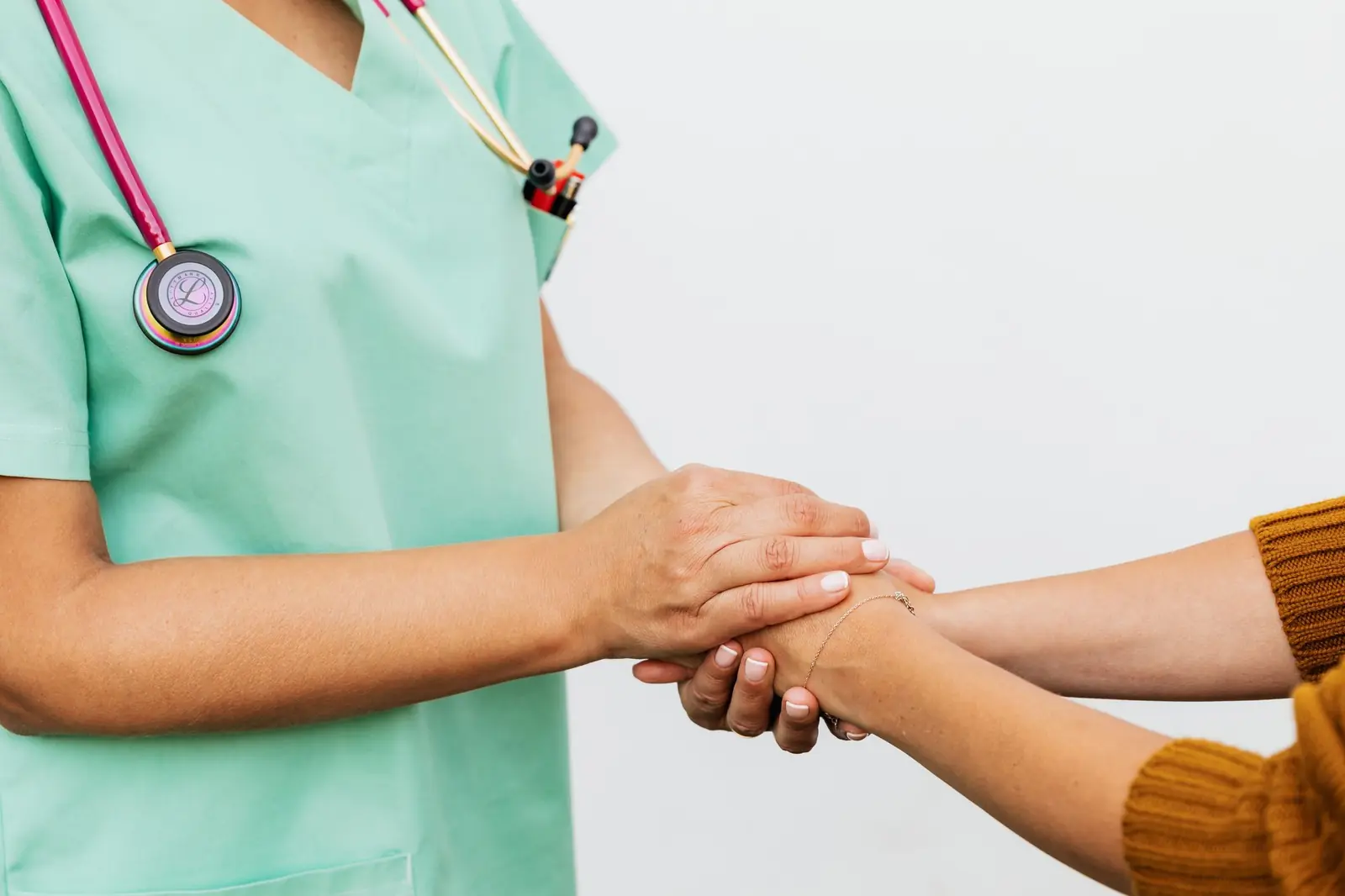 A clinician in teal scrubs gently holding a patient's hands in both of theirs