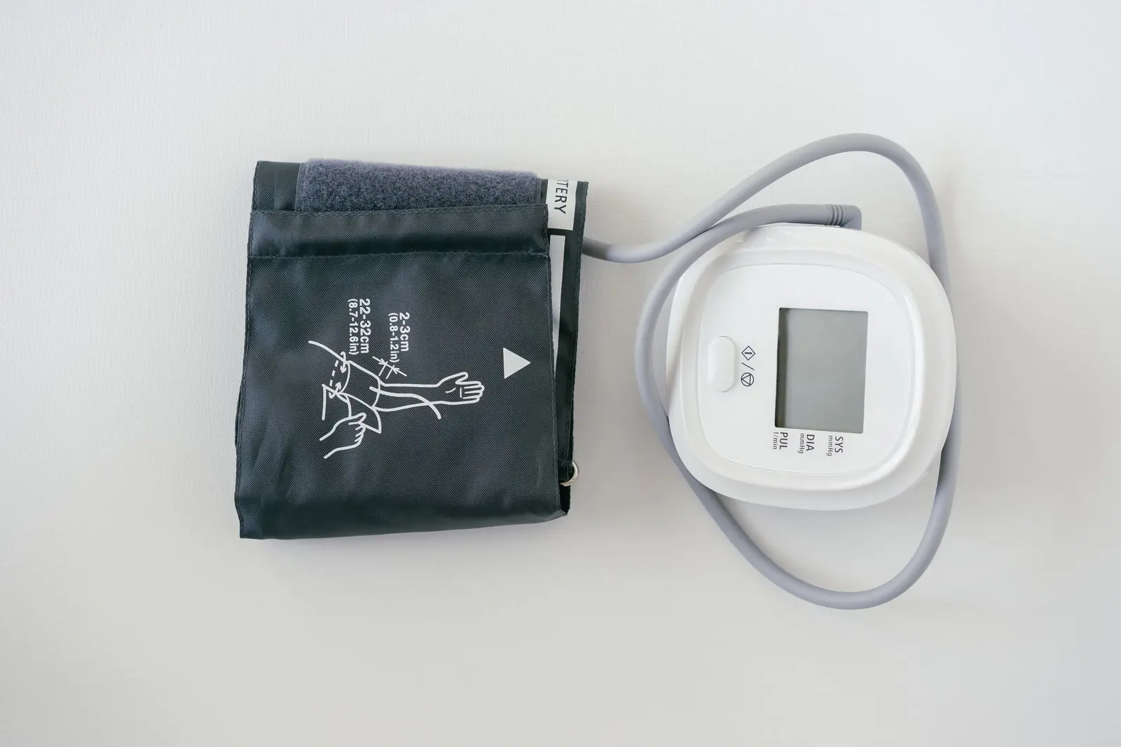 A digital blood pressure monitor and its folded arm cuff lying on a plain white surface