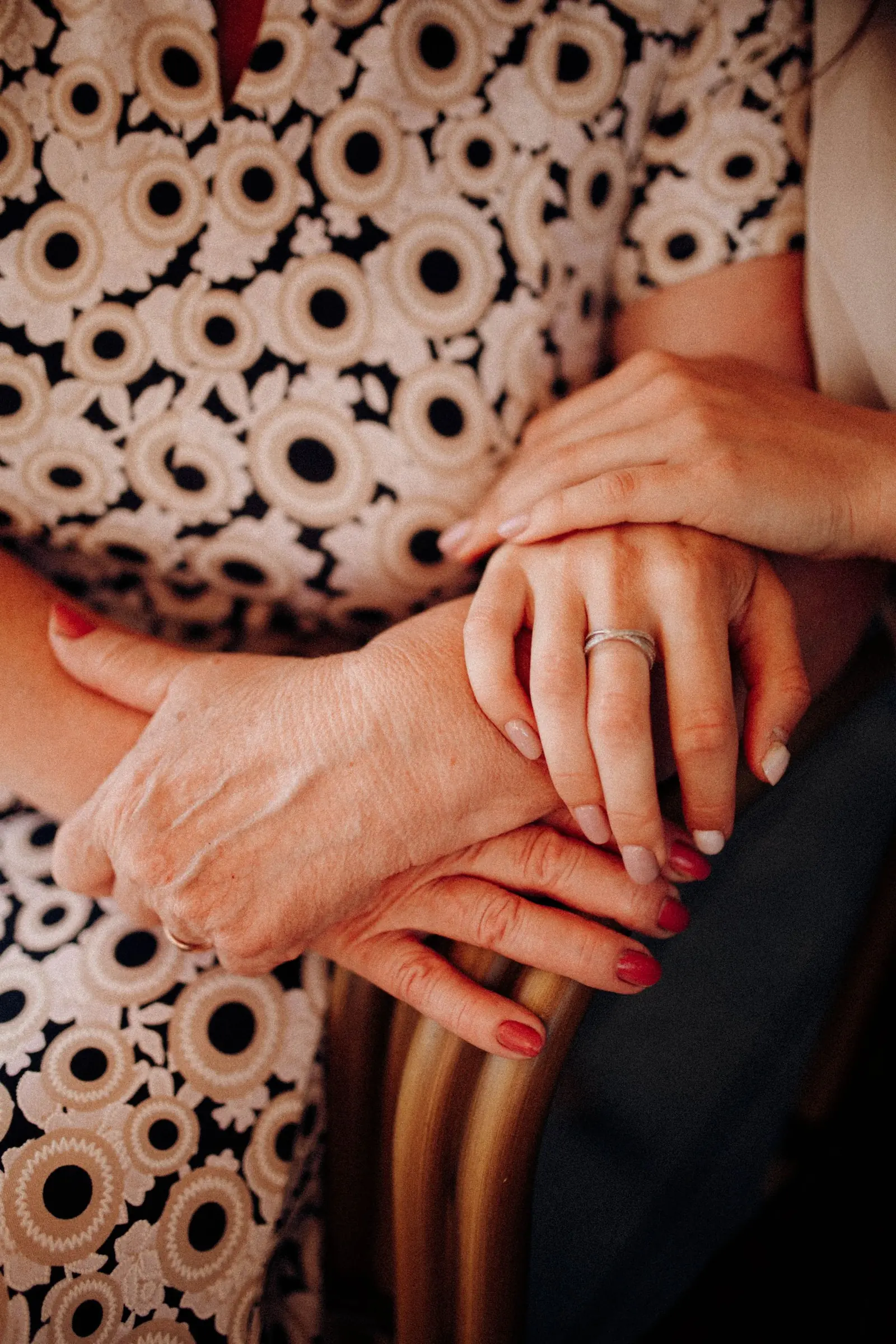 An adult daughter's hand resting over her mother's hands.