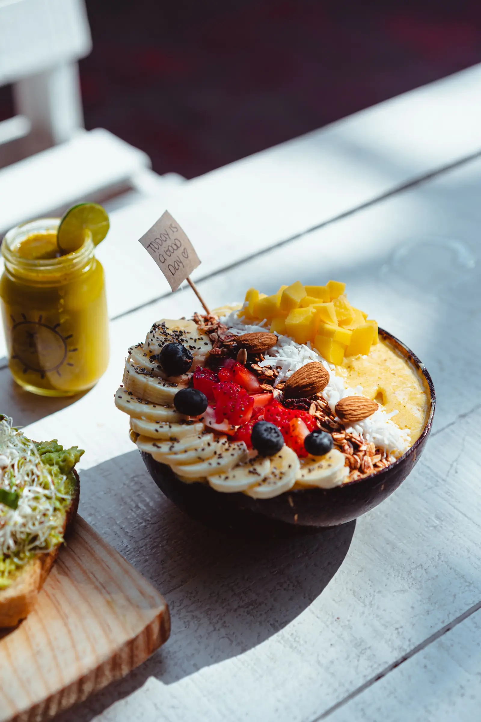 A breakfast bowl of fruit and nuts on a sunlit table.